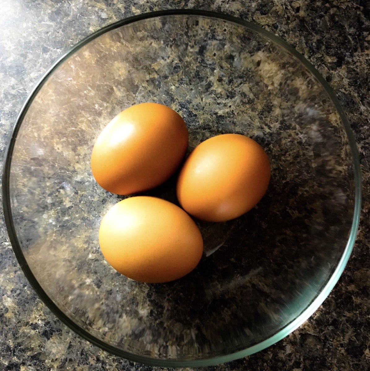 Three brown eggs in a glass bowl