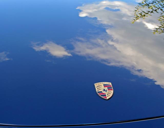 Porsche crest on a blue hood, clouds reflected